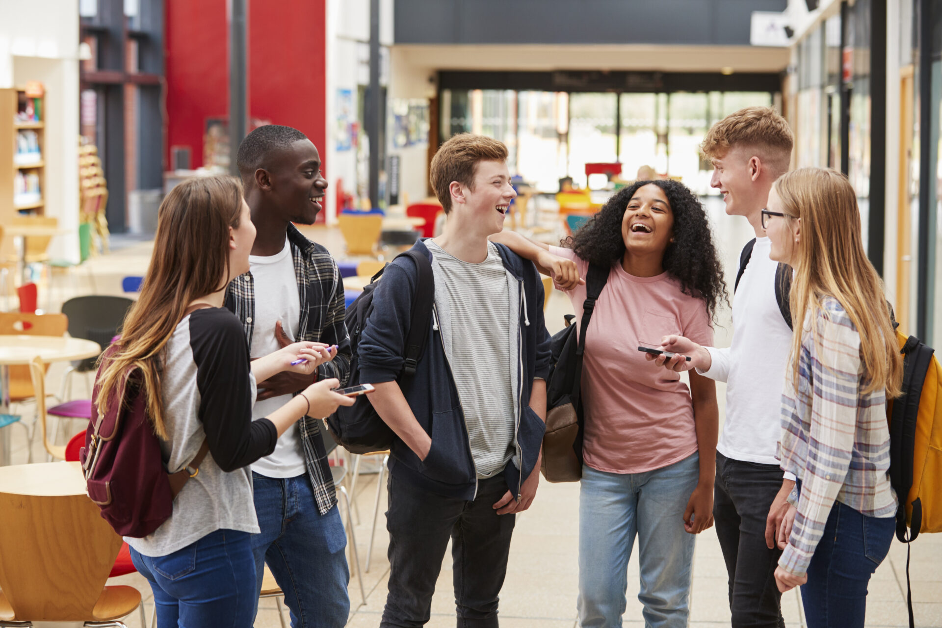 Groep van zes jongeren staan met elkaar op school te lachen.